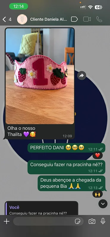 Print de conversa no WhatsApp com a cliente Daniela, mostrando a foto de uma coroa de feltro rosa com o número 1 em pink, morangos e florzinhas brancas, sobre uma mesa de madeira