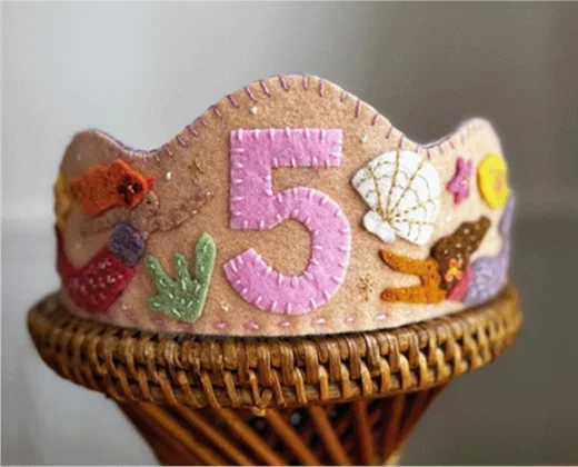 Coroa de feltro cru do tema sereia, com o número 5 em rosa na frente, conchas, coral e uma sereia aplicada