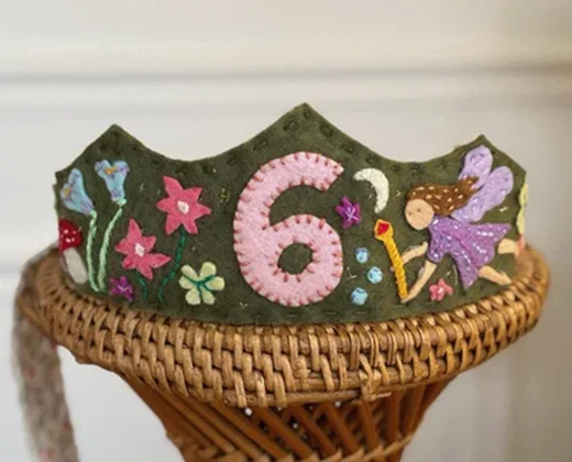 Coroa de feltro verde-musgo do tema fada, com o número 6 em rosa, flores, cogumelo e uma fada de asas lilás