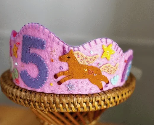 Coroa de feltro rosa do tema unicórnio, com o número 5 em roxo, um unicórnio dourado e estrelas